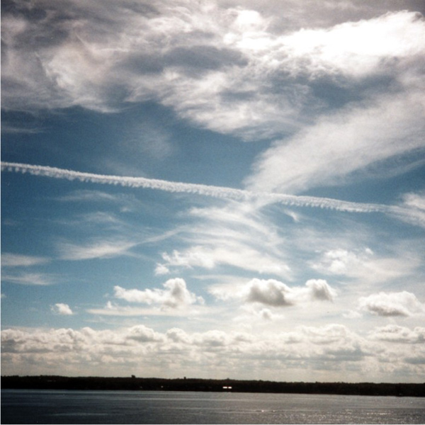 A large number of cumulus clouds above a lake, with sheets of cirrus and a jet aircraft contrail high above